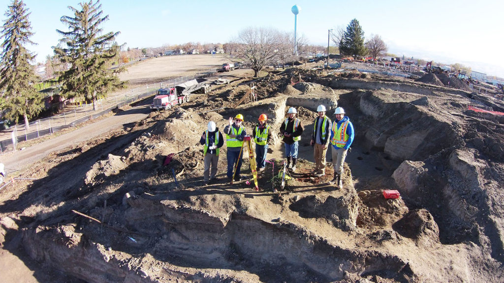 Photo of workers in the middle of a excavation site. They are wearing hi vis vests and helmets.