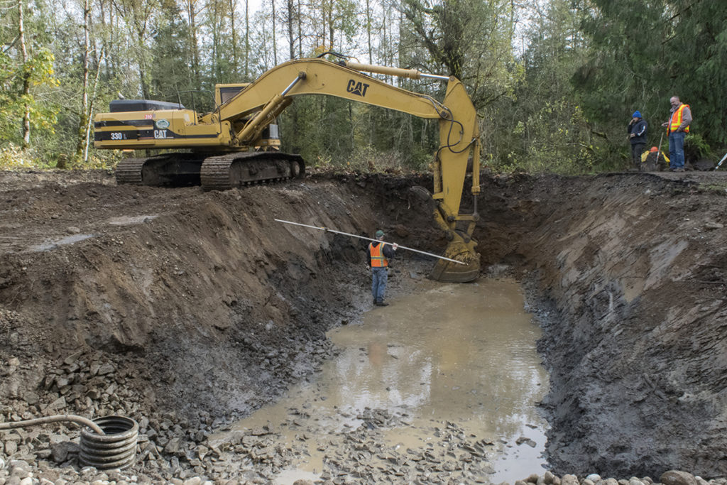 Photo of an excavator digging up a hole filled with water.