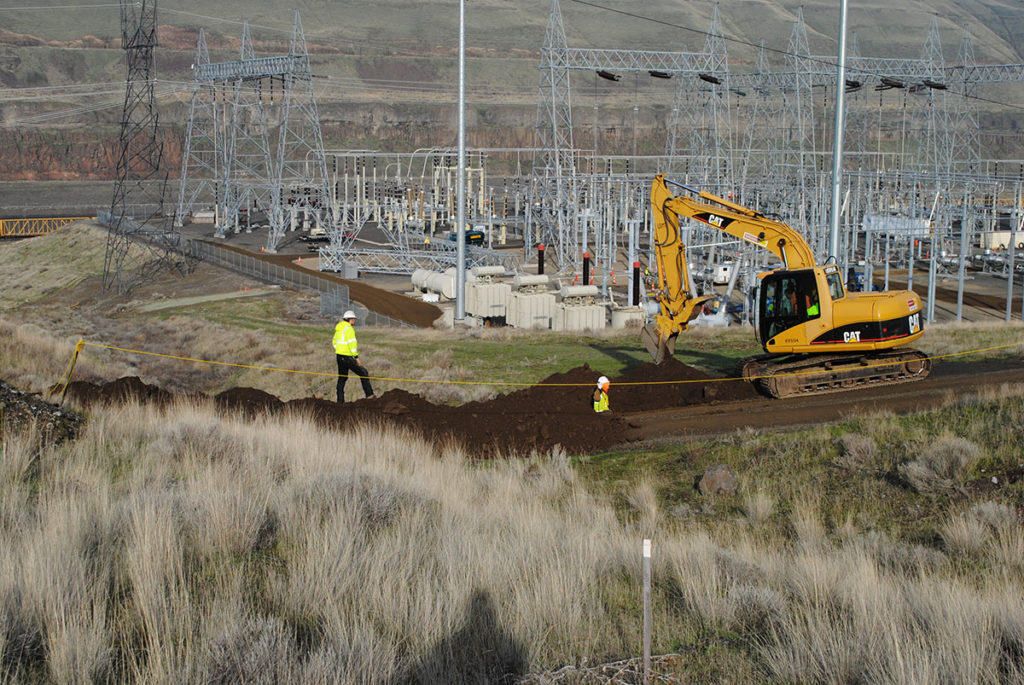 Far view of an excavation site. There two people in gear spotting for another working in a bulldozer