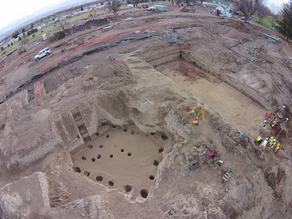 Aerial view of the Walla Walla ice house dig site. Workers have dug a large hole with smaller holes