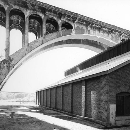 Old photo of a building under a bridge. The bridge is located far above the building