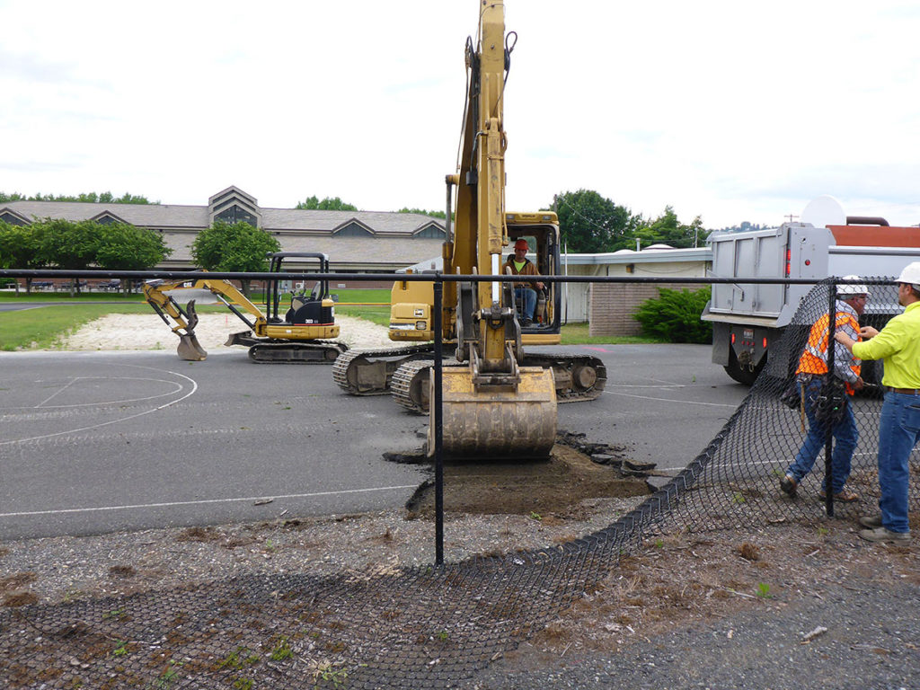 Photo of worker in an excavator digging up a road and two workers are by them.