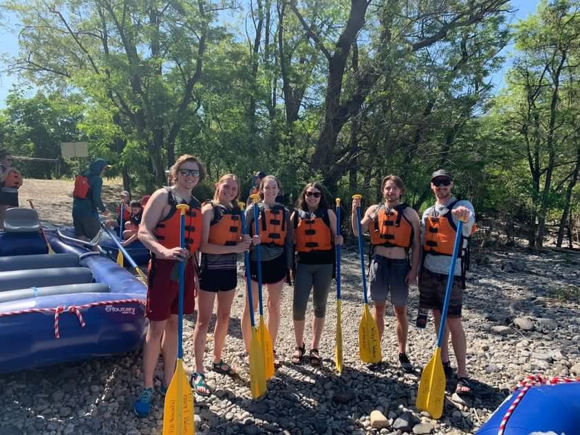 Group of people holding paddles and wearing life jackets in the summer