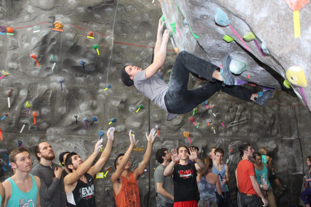 Man scaling climbing rock wall infront of a crowd