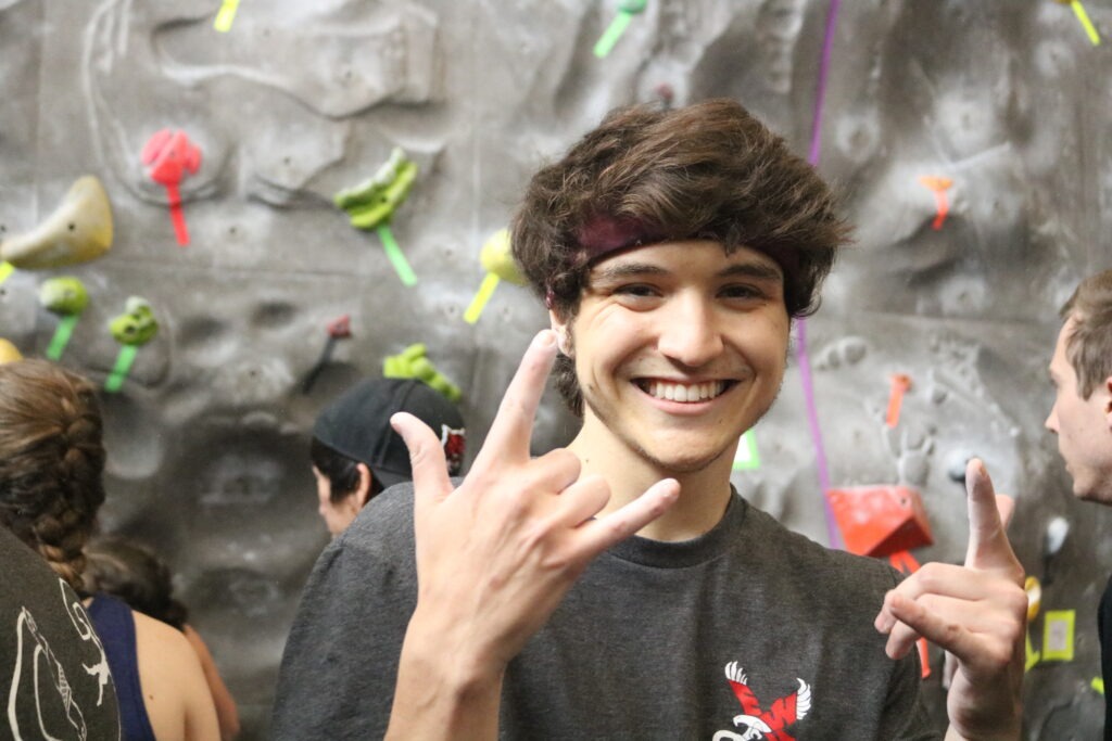 Man holding up a hang loose sign with his fingers in front of a rock wall