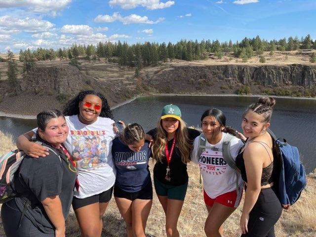 students with arms around each other shoulders behind lake