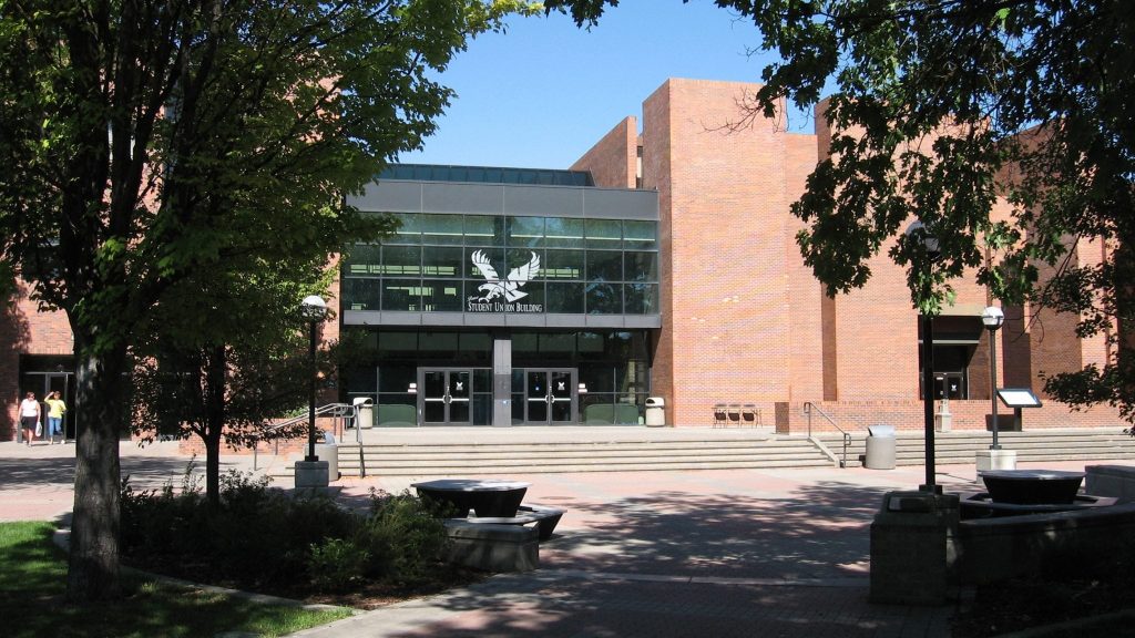 Pence Union Building photo from the front. It is in color and two trees are to each side of the building. On the front window of the PUB there is large white EWU logo