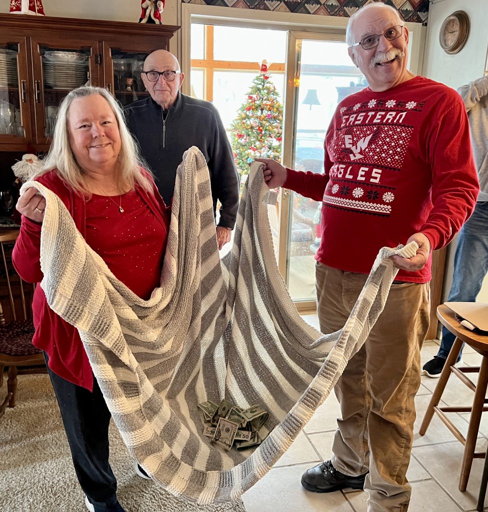 Three people holding a blanket with money in it