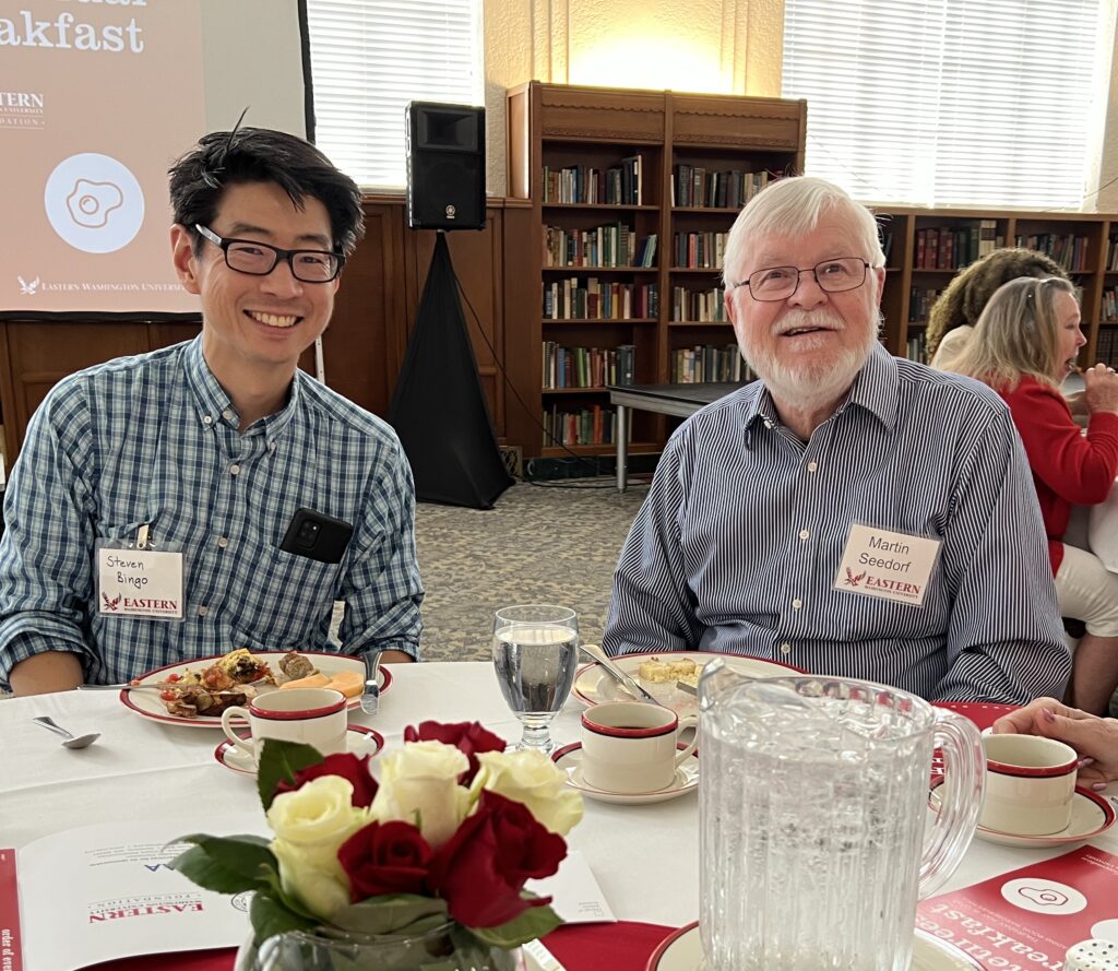 Two men sitting at a table, smiling at the camera