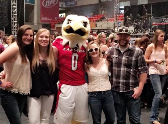 Group of people with arms around each other taking a photo with swoop. Swoop is the middle of the photo