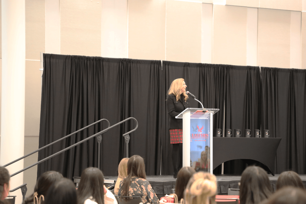 Women speaking at the SFL professional summit in front of a crowd on a stage. This is in the Nysether Community Room.